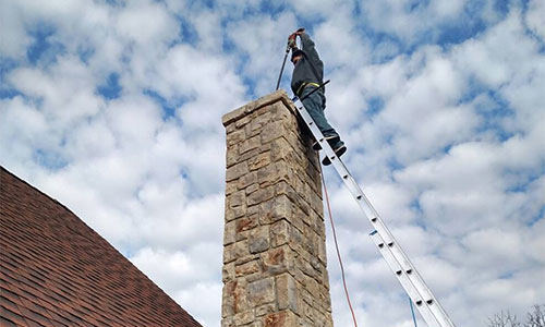 Chimney technician standing on a ladder against the chimney while deglazing it